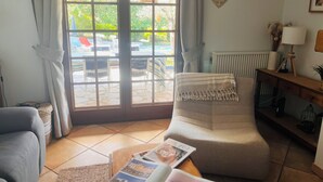 A living room with a sofa, a coffee table with magazines, a window with curtains, a radiator, and a wall-mounted heart decoration. - Charm and relaxed living in Lorgues: Villa Tira, swimming pool and 3300 m2 garden (Lorgues)
