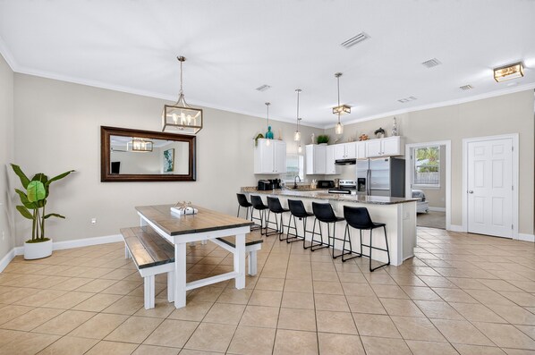 A modern kitchen with a central island, bar stools, and a dining table with benches.