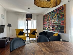 Una sala moderna con una mesa de comedor, sillones amarillos, un sofá negro y un cuadro abstracto colorido en la pared.