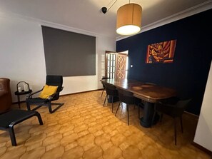 A room with a wooden floor, a dining table with chairs, a sofa, a small table with a lamp, and a painting on the wall. - 7 Bedroom house w/ 2 kitchens (Vila Nova de Gaia)