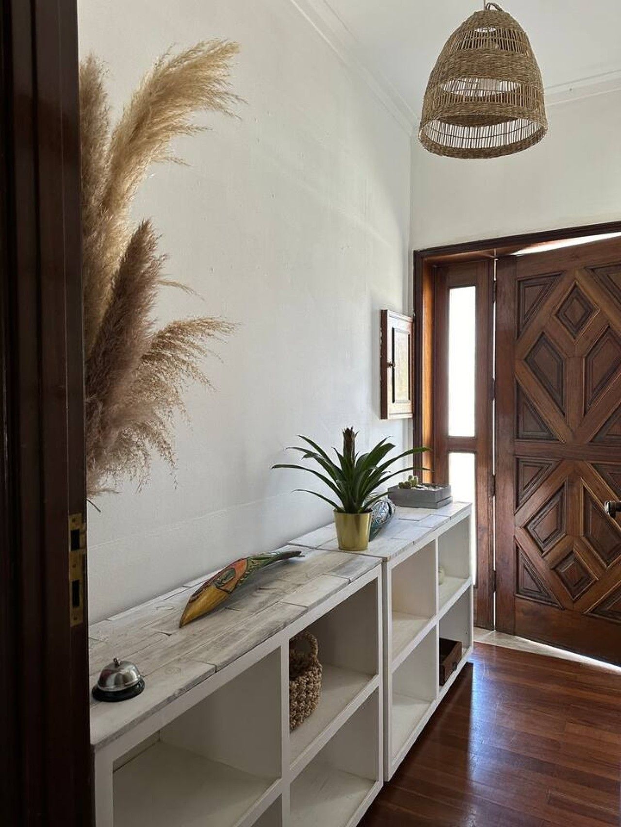 A hallway with a wooden door, a hanging light fixture, and a white console table with a plant and decorative items.