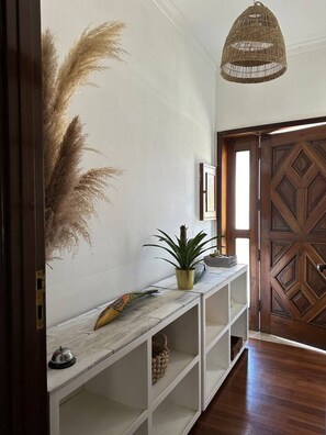 A hallway with a wooden door, a hanging light fixture, and a white console table with a plant and decorative items. - 7 Bedroom house w/ 2 kitchens (Vila Nova de Gaia)