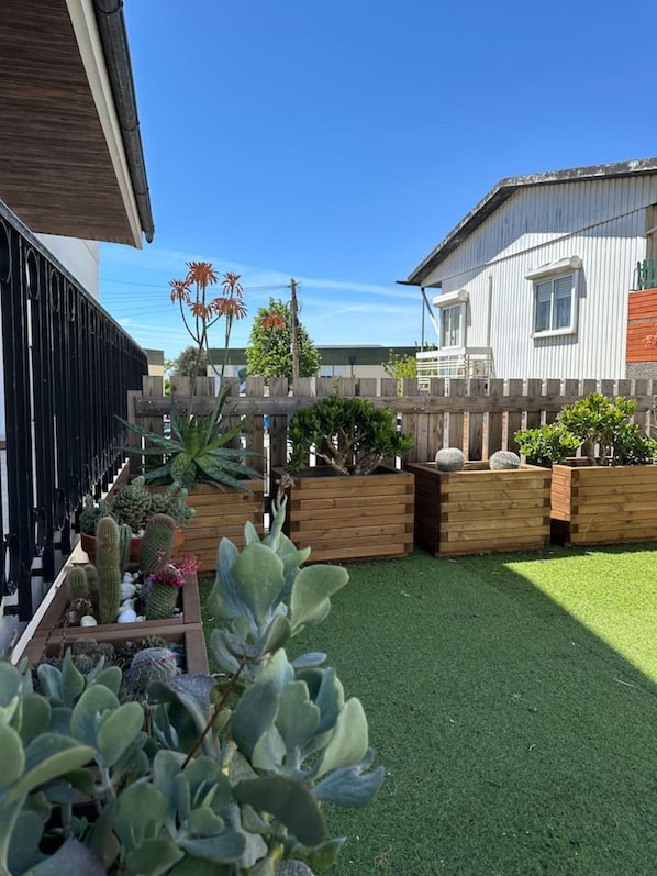 A residential property with a fenced backyard, various potted plants, and a well-maintained lawn.