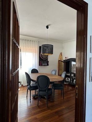 A dining area with a round wooden table and four chairs, a hanging lamp, and a dartboard on the wall.