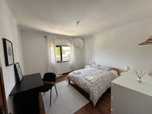 A bedroom with a bed, bedside table, chair, desk, and a window with curtains.