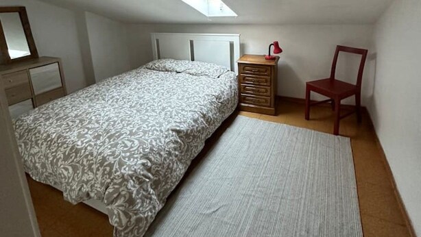 A small, single-bed room with a sloped ceiling, a bedside table with a lamp, a chair, and a mirror on the wall. - 7 Bedroom house w/ 2 kitchens (Vila Nova de Gaia)