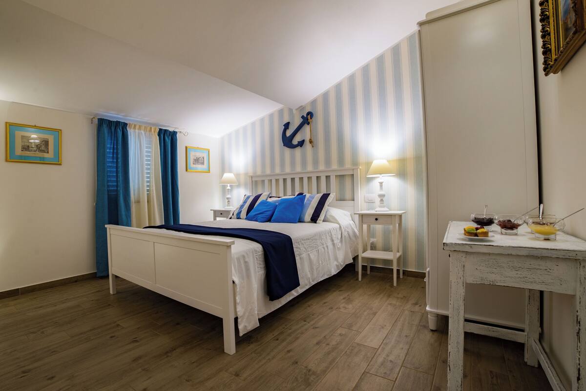 Une chambre à coucher comprenant un lit, des tables de chevet, une commode, une coiffeuse et une décoration murale en forme d’ancre.
