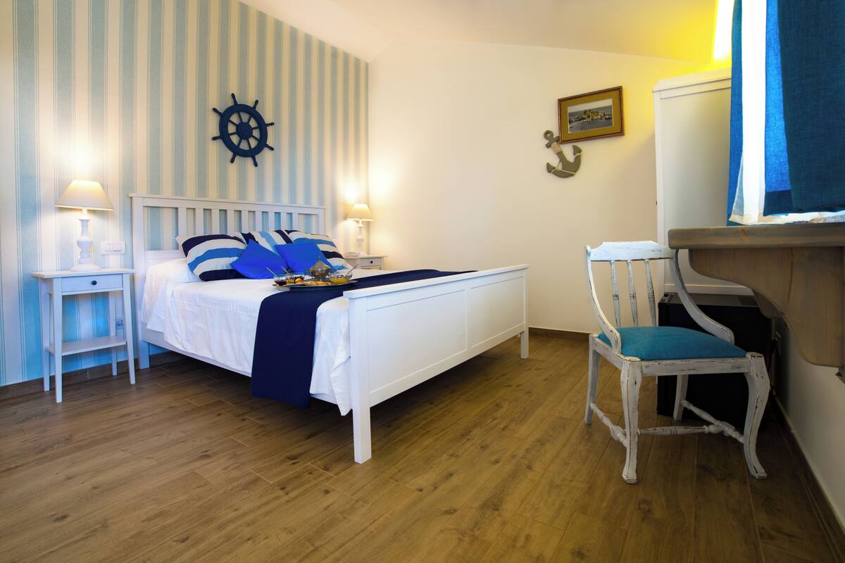 Une chambre à coucher comprenant un lit, des tables de chevet, une chaise, un gouvernail de bateau et un élément de décoration en forme d’ancre.