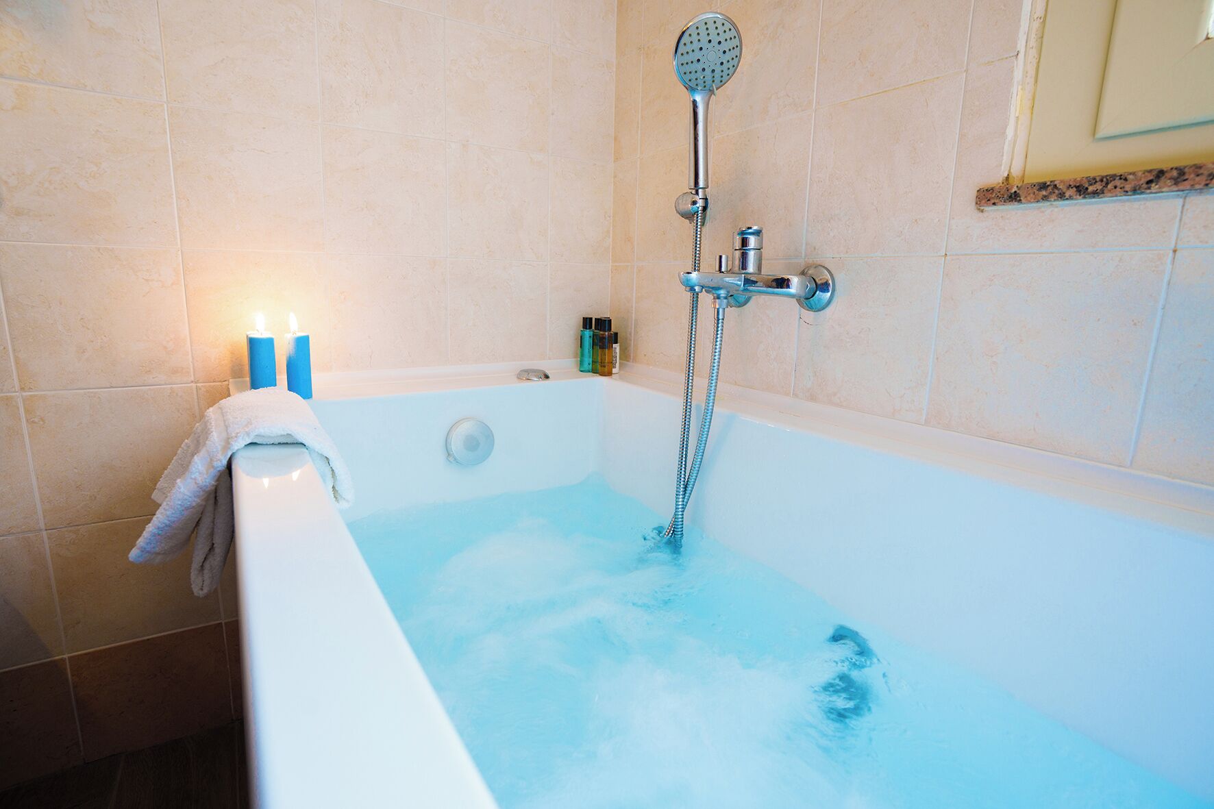 Un bagno con una vasca da bagno piena d'acqua, un soffione a mano e un asciugamano appeso al lato.