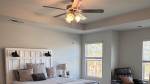Ein Schlafzimmer mit einem Bett, einem Sessel, einem Nachttisch und einem Deckenventilator.