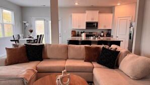 Ein modernes Wohnzimmer mit einem Ecksofa, einem Couchtisch und einer Küche im Hintergrund.