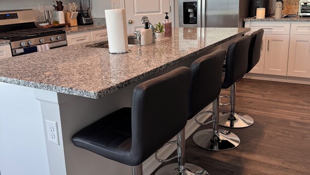 Eine moderne Küche mit weißen Schränken, einer Arbeitsplatte aus Granit, Edelstahlgeräten und einer Bar mit Hockern.