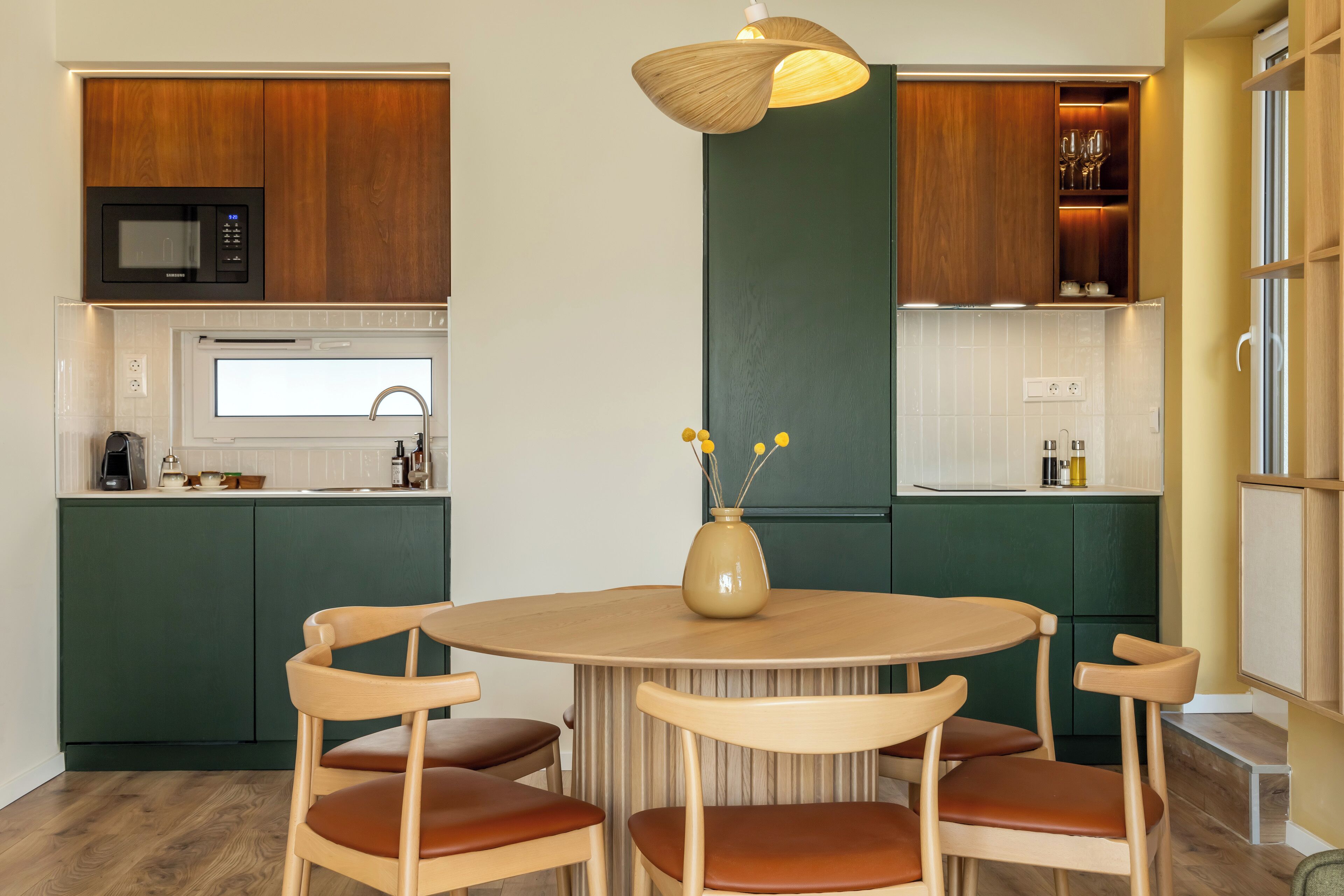 Une cuisine moderne avec des meubles en bois, une table à manger ronde et un vase rempli de fleurs.