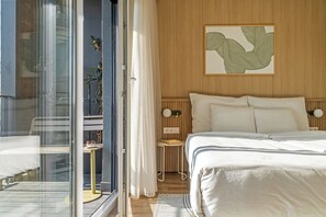 A hotel room with a bed, a small table with a lamp, a wall-mounted artwork, and a view through a glass door. - Marone Suites Budapest (Budapest)