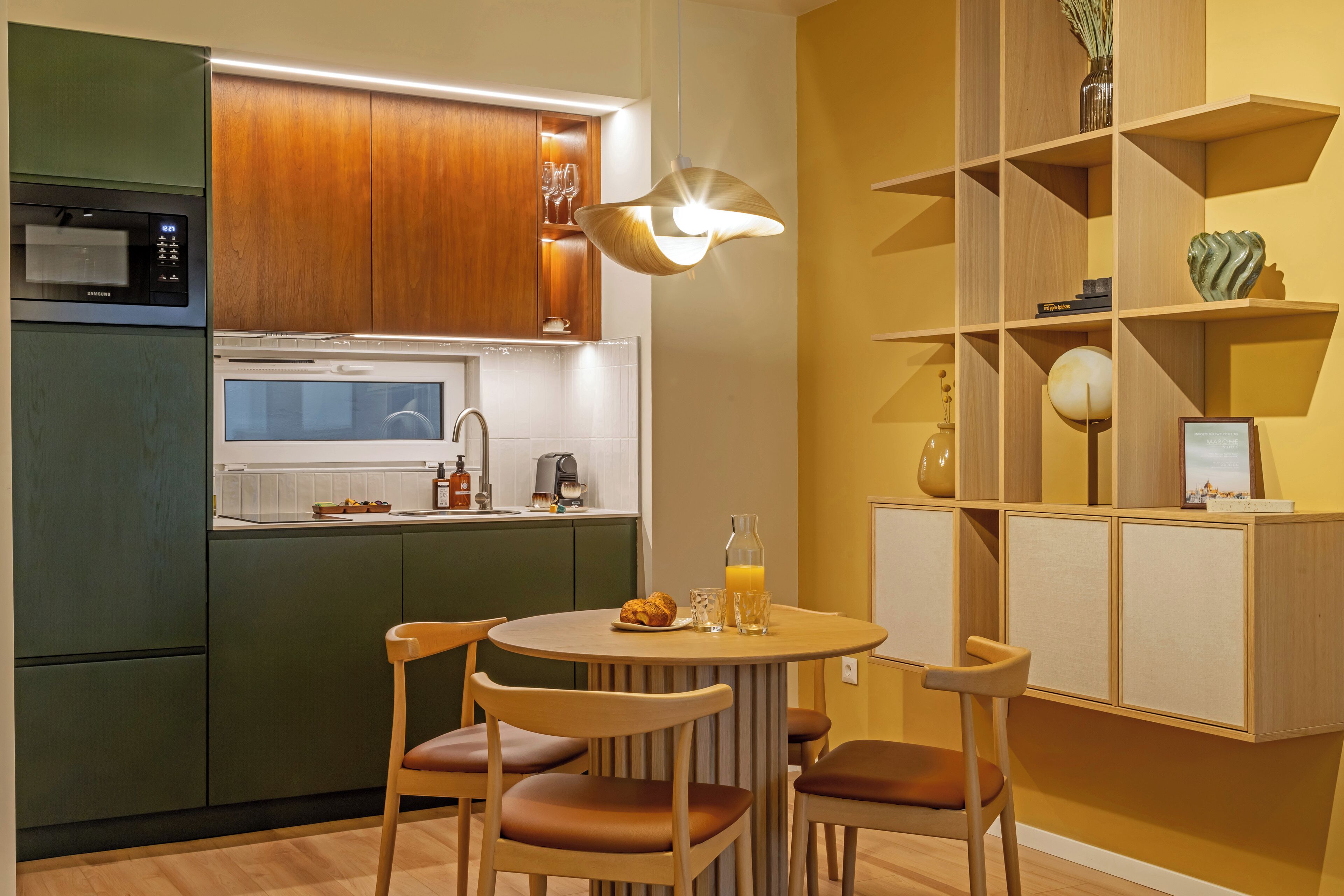 A modern kitchen with wooden cabinets, a built-in microwave, and a dining area with a round table and chairs.