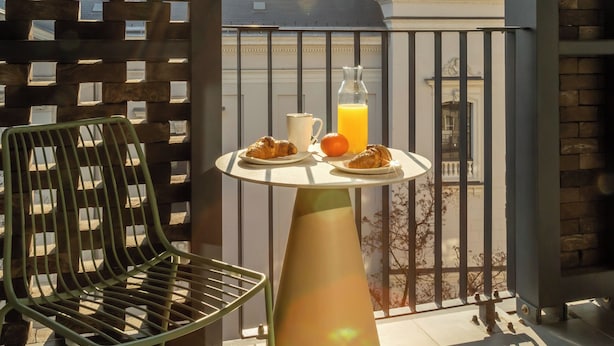 A balcony with a table set for breakfast, a chair, and a view of a historic building with a clock. - Marone Suites Budapest (Budapest)