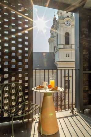 A balcony with a table set for breakfast, a chair, and a view of a historic building with a clock. - Marone Suites Budapest (Budapest)