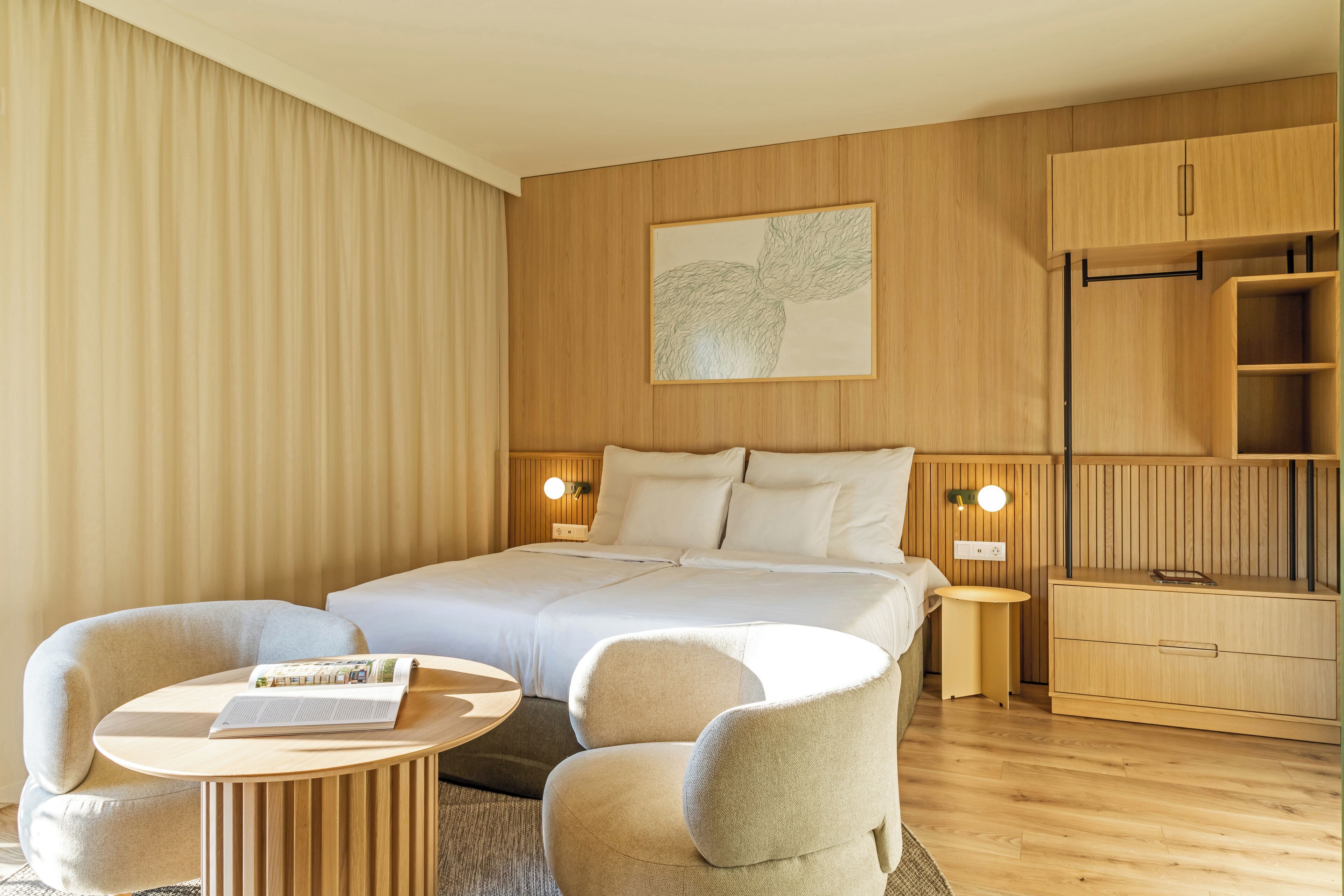 Une chambre d’hôtel moderne, dotée d’un grand lit, de deux tables de chevet, d’une petite table ronde et de deux fauteuils.