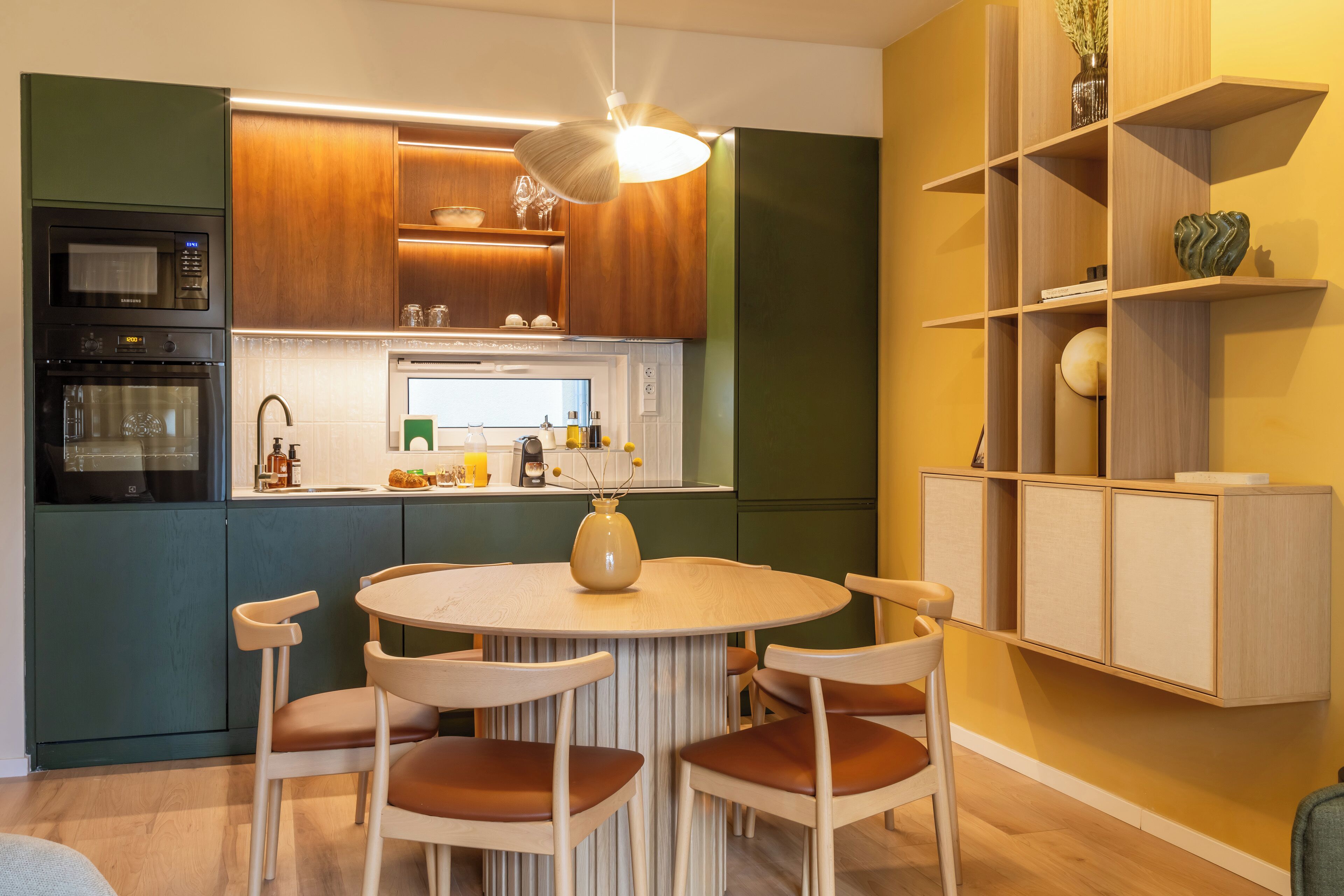 A modern kitchen with wooden cabinets, a built-in oven, and a dining area with a round table and chairs.