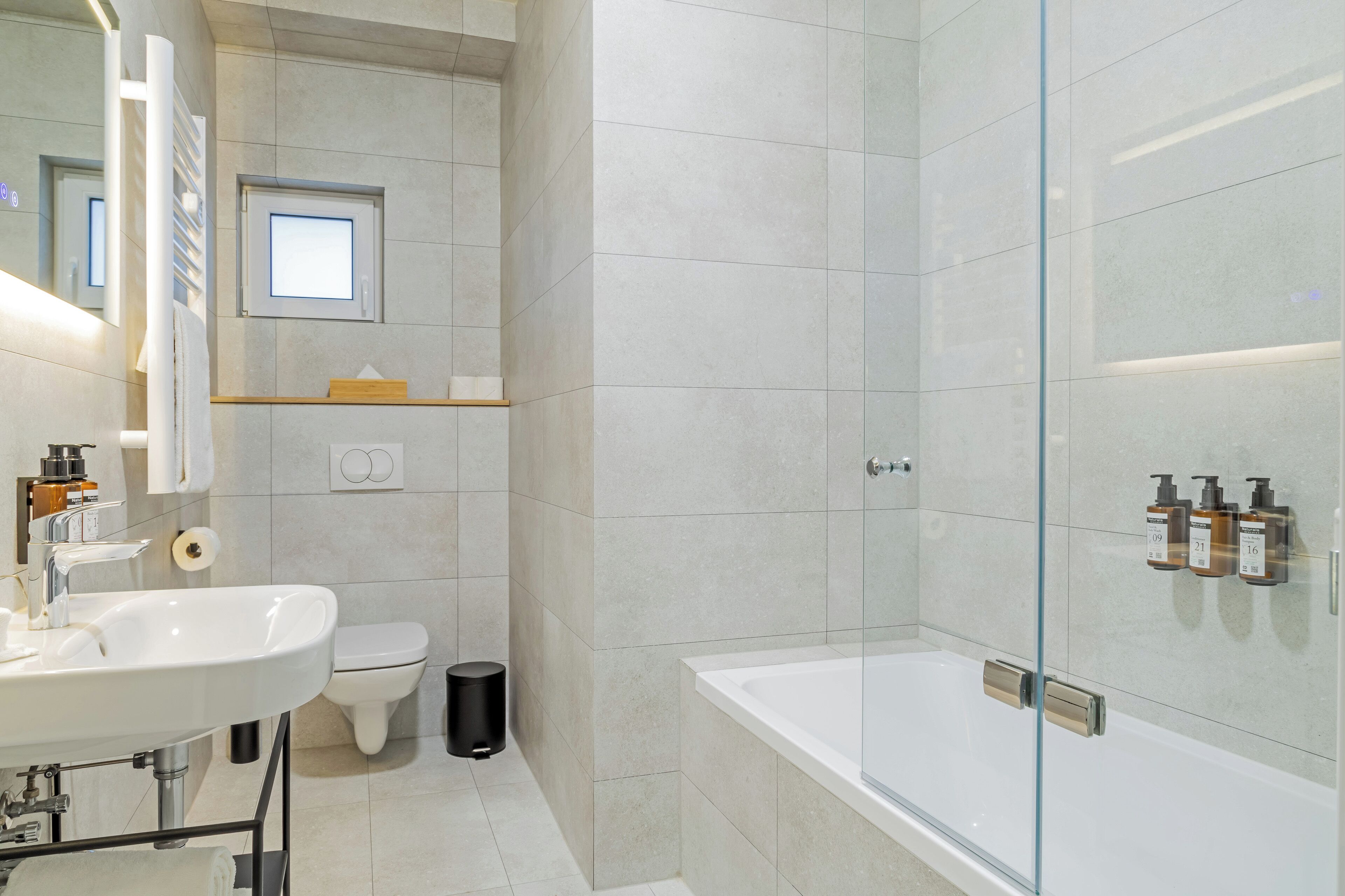 A modern bathroom with a white sink, toilet, and glass-enclosed shower area.