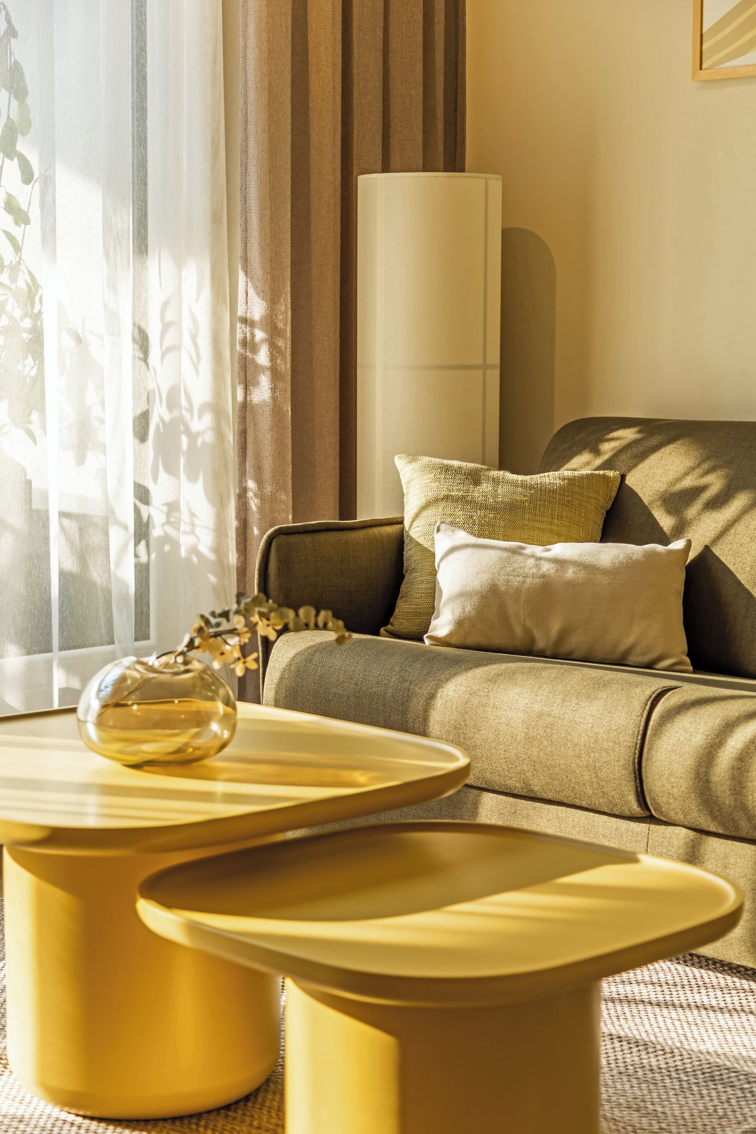 A modern living room with a sofa, two round yellow side tables, and a vase on one table.