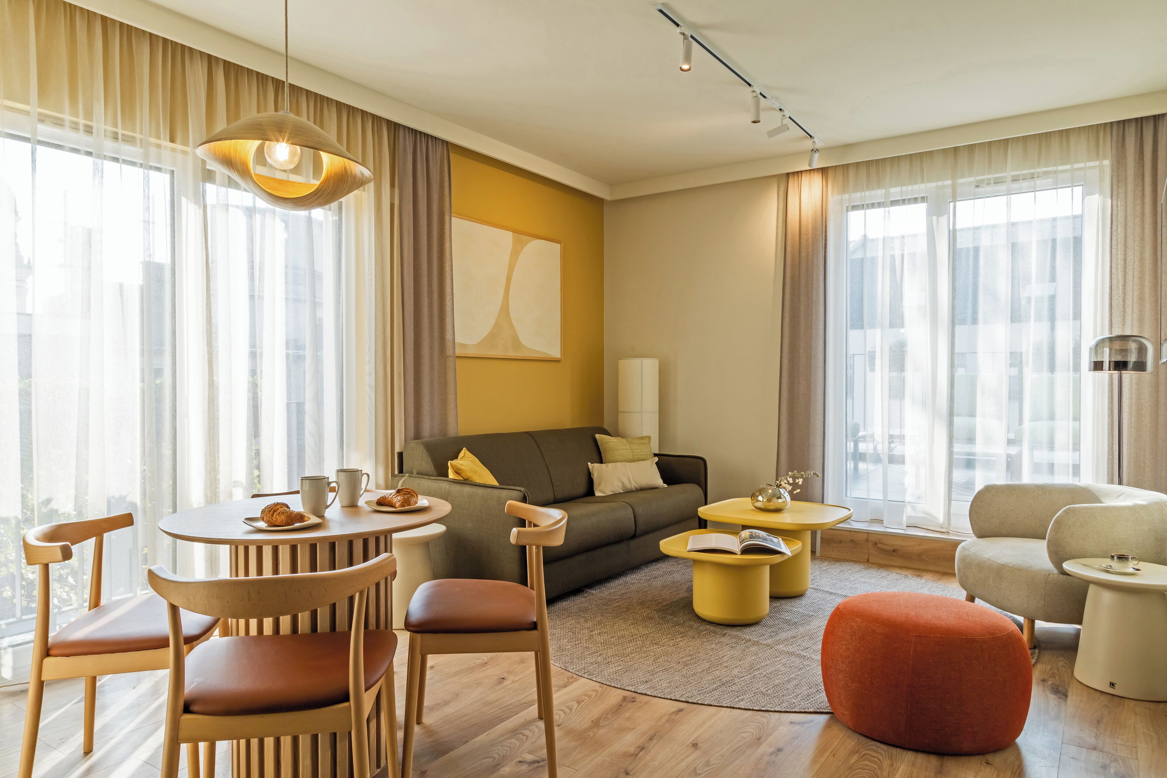 A modern living room with a sofa, chairs, a coffee table, and a round table with a lamp.