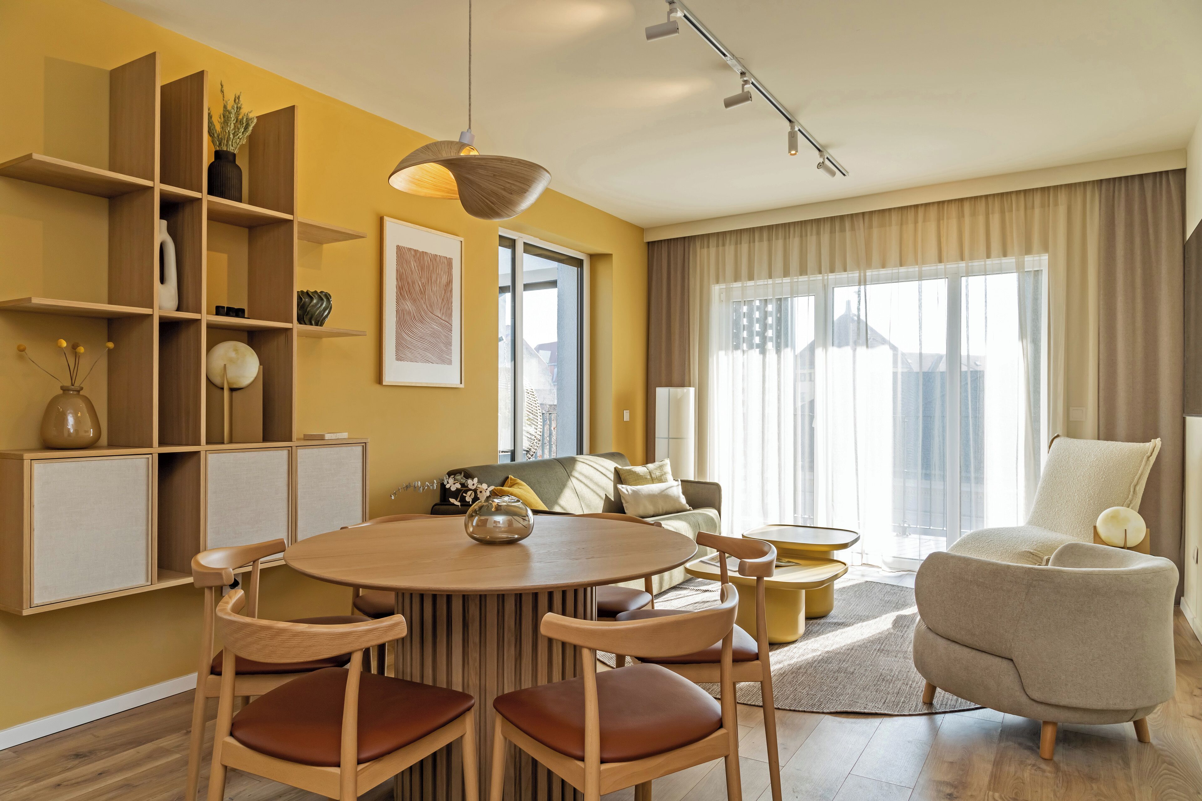 Un salon moderne avec une table ronde en bois, des chaises assorties, un canapé et une grande fenêtre avec des rideaux.
