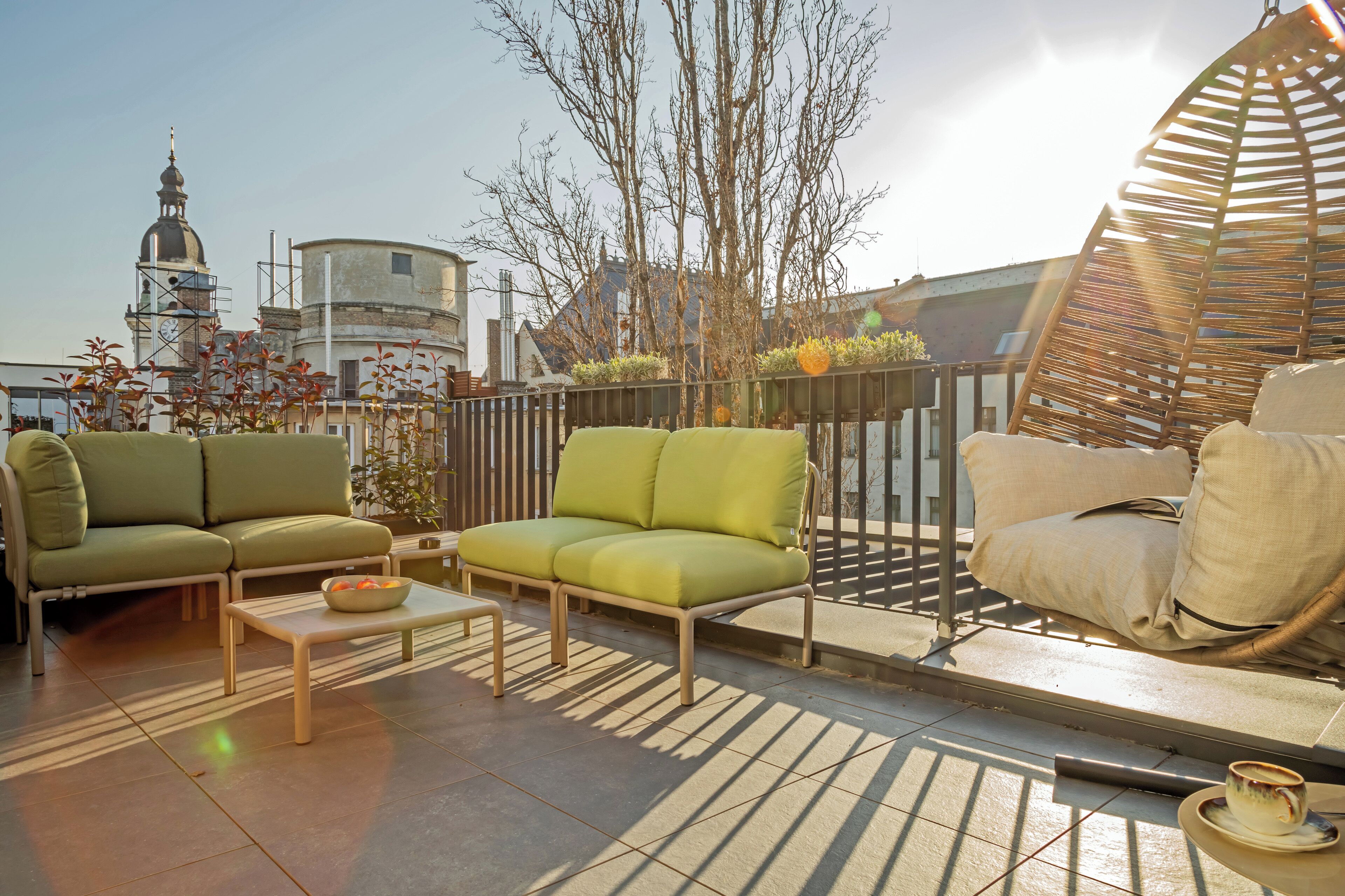A rooftop terrace with a green sofa set, a small table with a bowl, and a wicker chair.