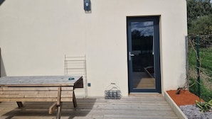 Eine Holzterrasse mit Tisch und Stühlen, einer Tür und einem kleinen Gartenbereich mit Pflanzen.