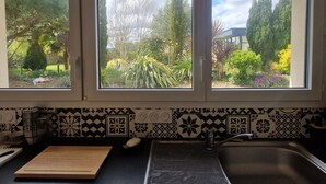 Eine Küche mit Blick auf einen Garten durch drei Fenster, inklusive Spüle und einem gemusterten Küchenrückwand.