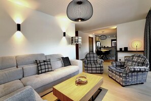 Ein modernes Wohnzimmer mit einem grauen Sofa, Karo-Sesseln und einem Holztisch.