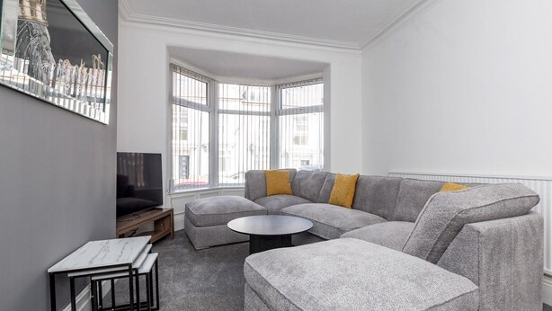 Ein modernes Wohnzimmer mit einem grauen Ecksofa, einem runden Couchtisch und einem Fernseher auf einem Holzboden.