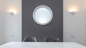 Ein Konferenzraum mit einem Marmortisch, zwei Ledersesseln, einem runden Spiegel und Wandleuchten.