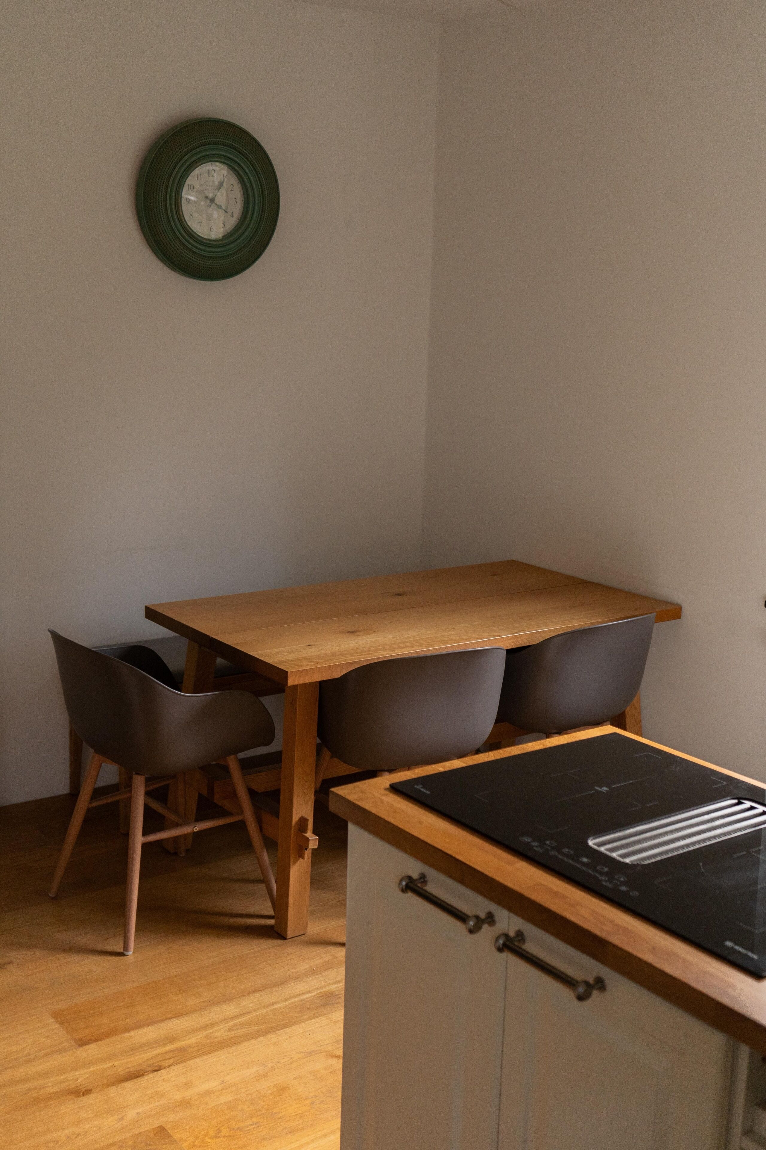 Un petit coin repas avec une table en bois et deux chaises, une plaque de cuisson à induction noire et une horloge verte accrochée au mur.