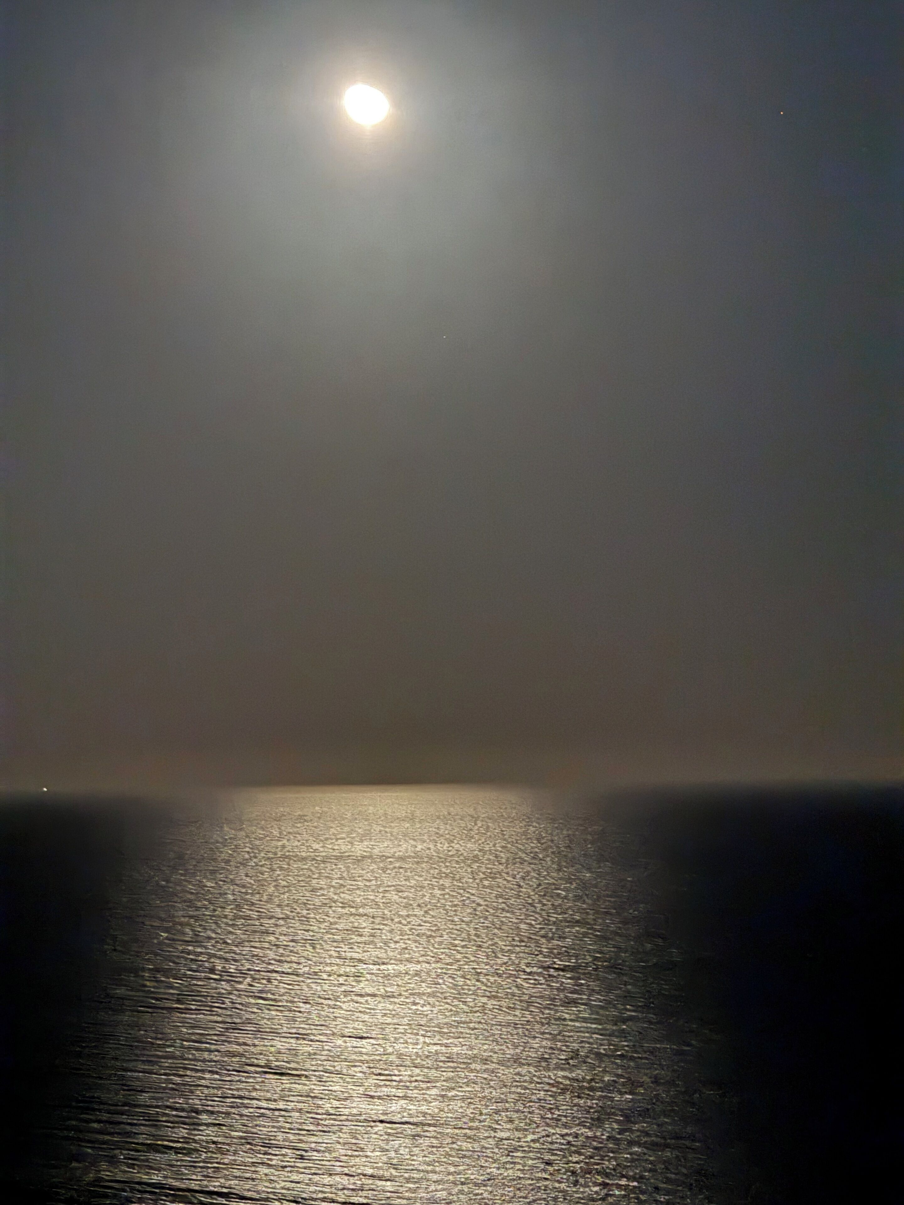 A night scene with a full moon reflecting on calm water.