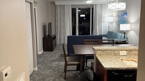 Kompakti hotellihuone, jossa on pieni keittiö, ruokailutila ja oleskelualue.