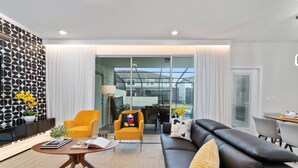 A modern living room with a black leather sofa, yellow armchairs, and a round coffee table. - Themed 5BR Home w/ Pool · Windsor Island Resort (Davenport)