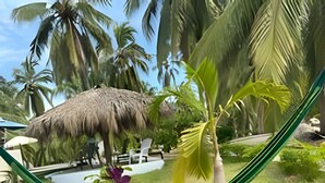 Una mesa de madera con un florero, una hamaca y vistas a una piscina y palmeras.