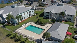 Et boligområde med en swimmingpool omgivet af liggestole, en indhegnet terrasse og en lille bygning med rødt tag.
