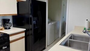Et lille køkken med et sort køleskab, en kaffemaskine og en stålvask.