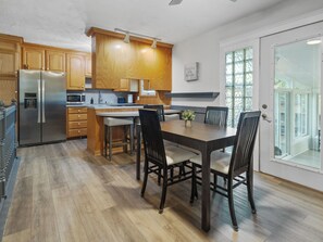 A modern kitchen with wooden cabinets, a stainless steel refrigerator, and a dining area with a table and chairs. - Bright & Cozy Home - Sunroom, Games & Foosball in La Vista, NE (La Vista)