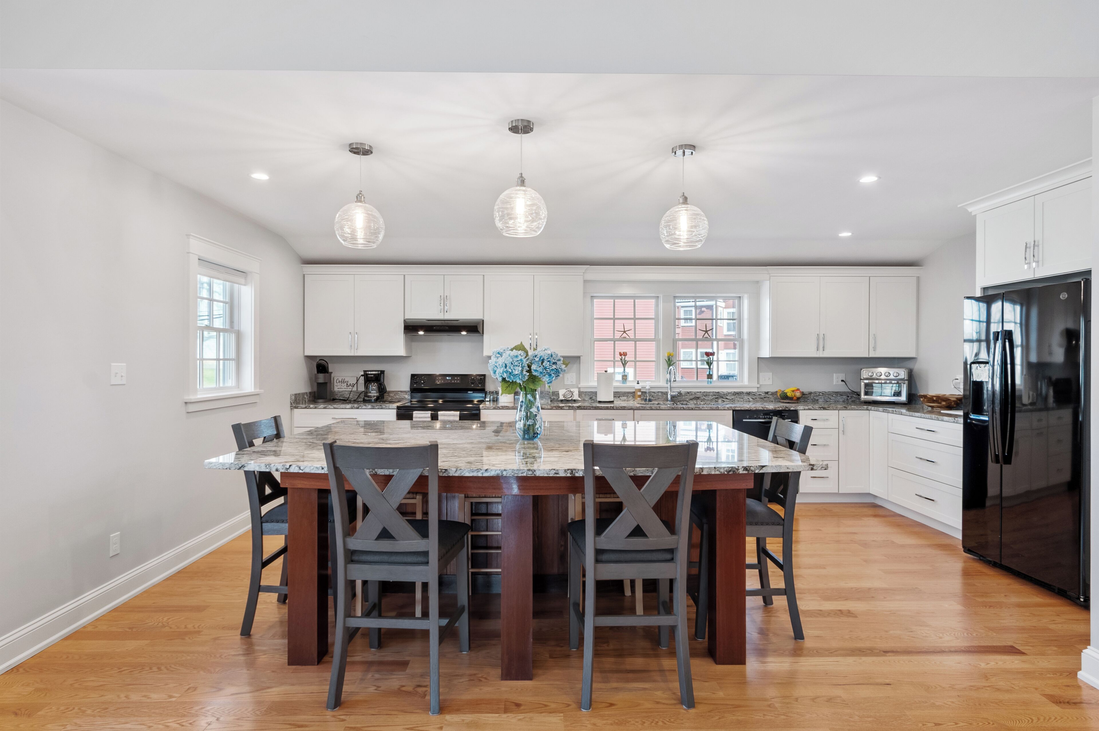 Une cuisine moderne avec des meubles blancs, un îlot central, des luminaires suspendus et un réfrigérateur noir.