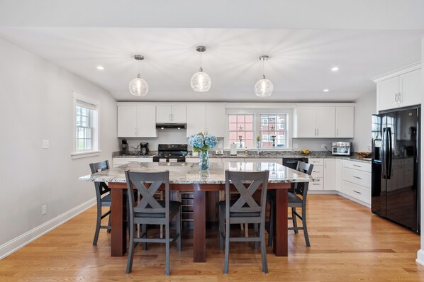 A modern kitchen with white cabinets, a central island, pendant lighting, and a black refrigerator.