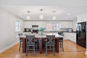 A modern kitchen with white cabinets, a central island, pendant lighting, and a black refrigerator.