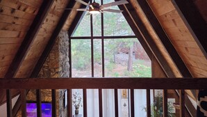 Ein Zimmer mit schrägverlegtem Holzboden, einem Deckenventilator und einem großen Fenster mit Blick ins Freie.