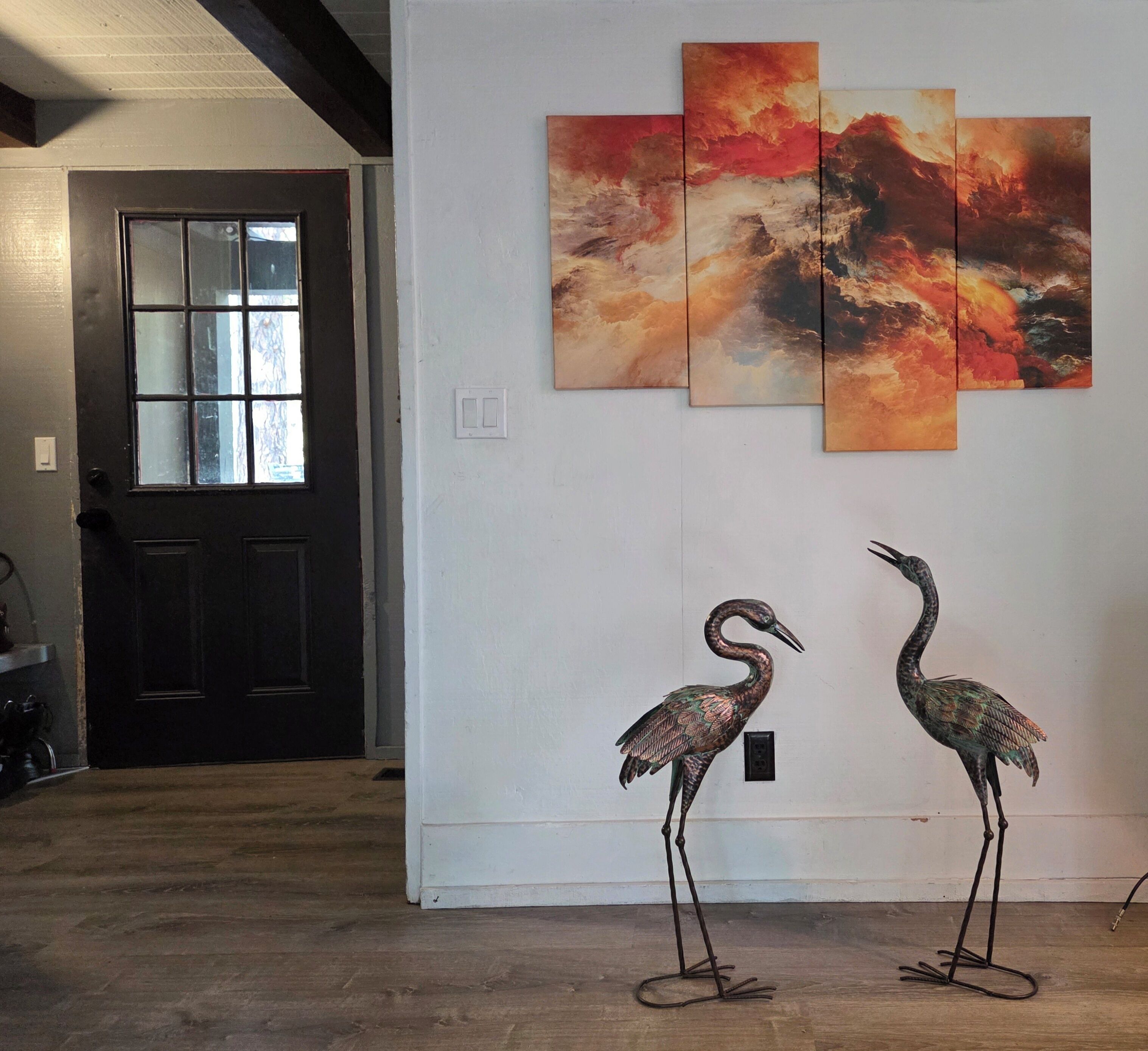 A room with a wooden floor, a black door, and a wall with three paintings.