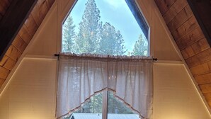 Ein Schlafzimmer mit großem Fenster, einem Bett mit weißer Bettwäsche, zwei Nachttischen mit Lampen und einer Holzbodenverkleidung.