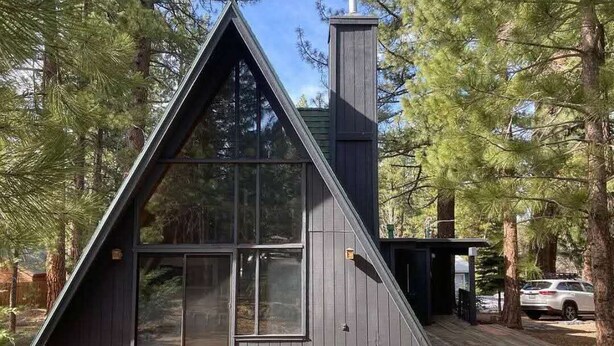 Ein modernes A-Haus mit großen Fenstern und Schornstein, umgeben von Bäumen.