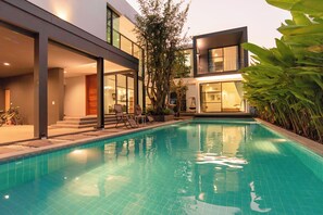 Una casa moderna amb piscina, finestres grans i mobiliari per a l'exterior.