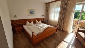 Een slaapkamer met een houten bed, een nachtkastje, een raam met gordijnen en uitzicht op groen.